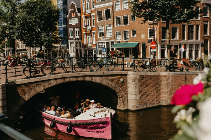 Een roze rondvaartboot vaart onder een boogbrug door op een Amsterdamse gracht